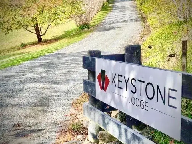 The gravel driveway and Keystone Lodge sign on the black wooden fence at the entrance.