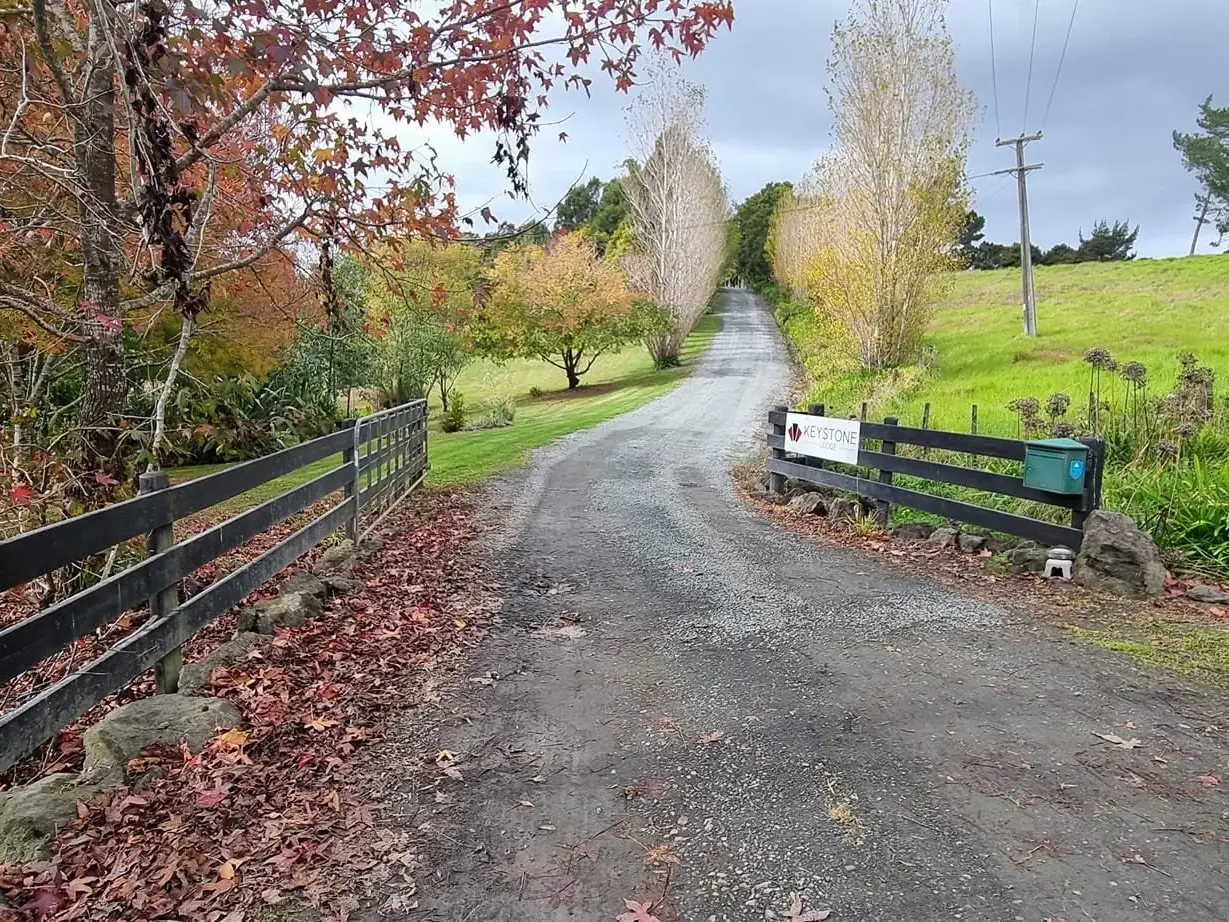 A gravel country road with trees on either side, a wooden fence on the left and a sign for Keystone Office on the right.