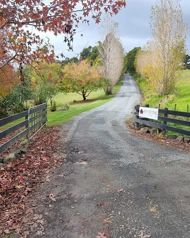 A gravel country road with trees on either side, a wooden fence on the left and a sign for Keystone Lodge Office on the right.