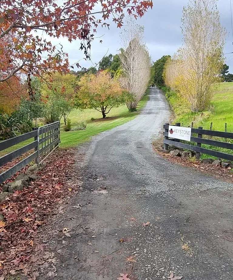 A gravel country road with trees on either side, a wooden fence on the left and a sign for Keystone Office on the right.
